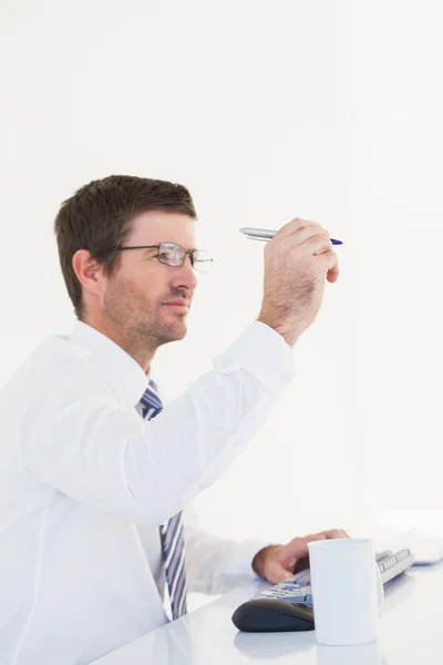 Businessman holding pen up at desk — Stock Photo, Image