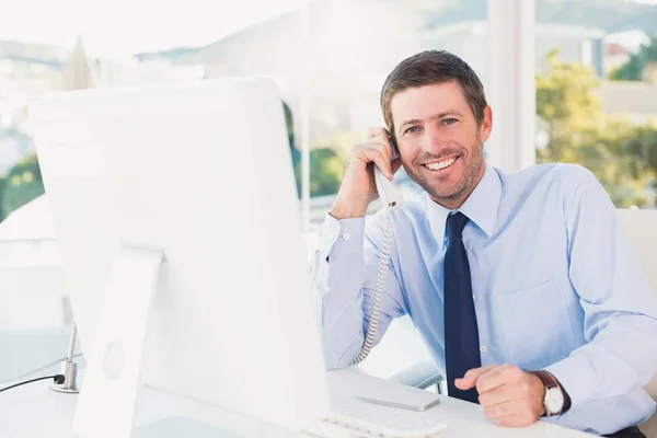 Homem de negócios sorrindo telefonando para sua mesa — Fotografia de Stock