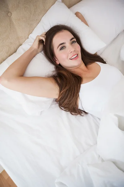 Ładna brunetka leżąc w łóżku, uśmiecha się do kamery — Zdjęcie stockowe