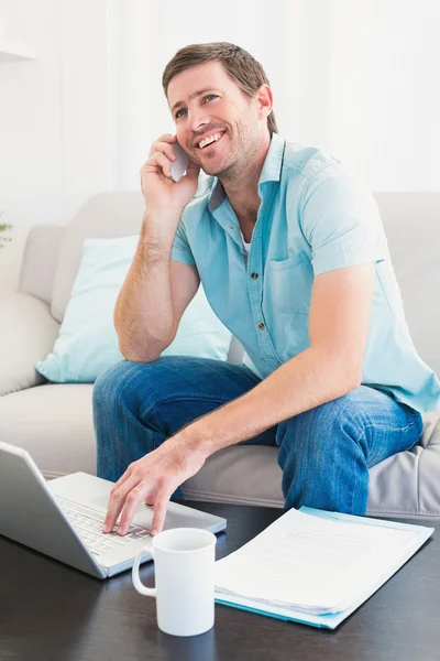 Sorrindo homem em um telefone com um laptop em casa — Fotografia de Stock