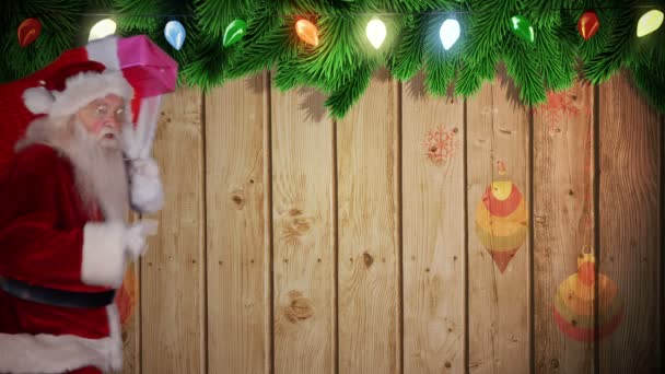 Santa uitvoering zak van giften tegen feestelijke houten achtergrond — Stockvideo