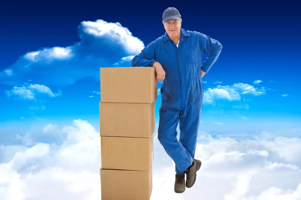 Happy delivery man leaning on pile of cardboa — Stock Photo, Image