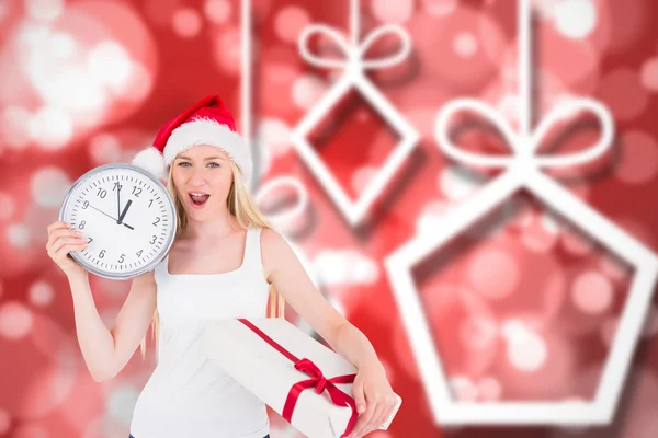 Composite image of festive blonde holding a clock and gift — Stock Photo, Image