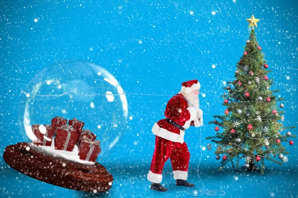 Composite image of santa pulling snow globe of presents — Stock Photo, Image