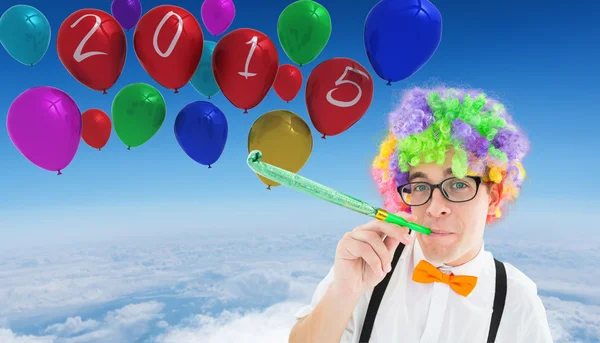 Geek blowing party horn against balloons — Stock Photo, Image