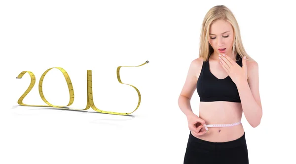 Composite image of fit young blonde looking at measuring tape — Stock Photo, Image