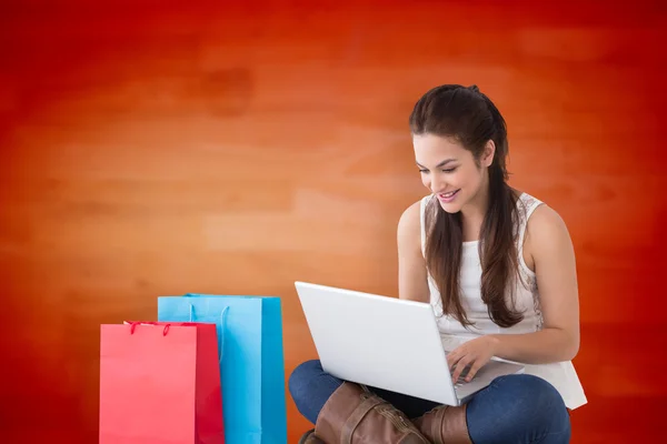 Imagem composta de morena sorridente sentada e usando seu laptop — Fotografia de Stock