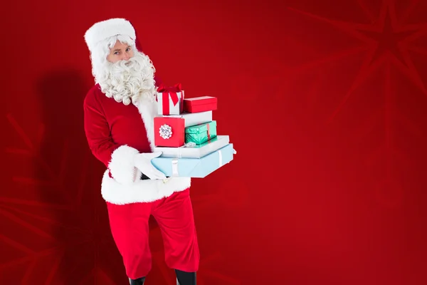 Imagen compuesta de Papá Noel sosteniendo muchos regalos — Foto de Stock