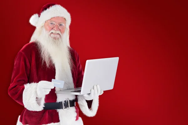 Santa paga con tarjeta de crédito en el ordenador portátil — Foto de Stock