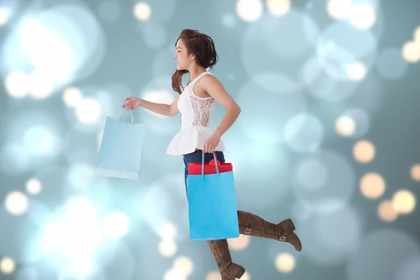 Imagem composta de morena feliz pulando com sacos de compras — Fotografia de Stock