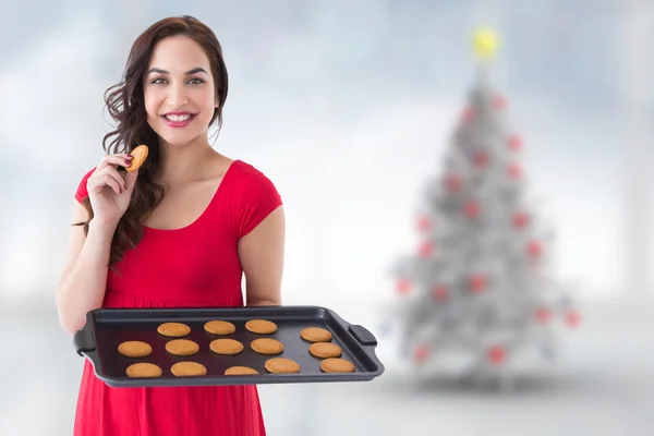 Composite image of happy brunette eating hot cookies — Stock Photo, Image