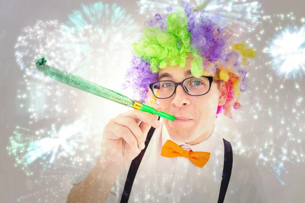 Geeky hipster φορώντας ένα ουράνιο τόξο περούκα φυσώντας κόμμα — Φωτογραφία Αρχείου