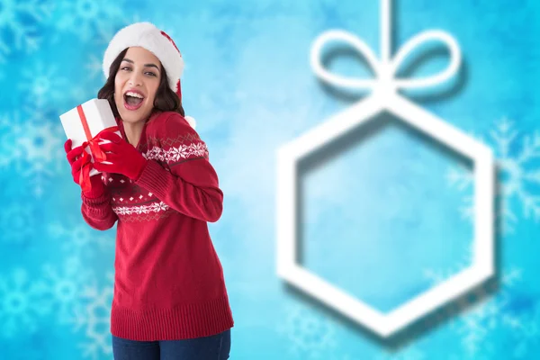Composite image of excited brunette showing christmas present — Stock Photo, Image