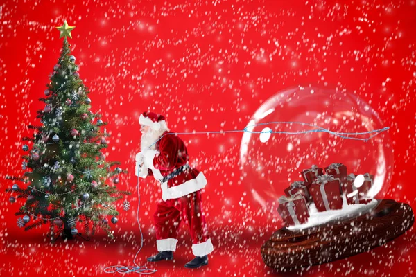 Composite image of santa pulling snow globe of presents — Stock Photo, Image