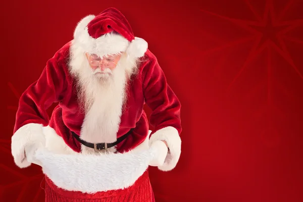 Samengestelde afbeelding van santa kijkt in zijn zak — Stockfoto