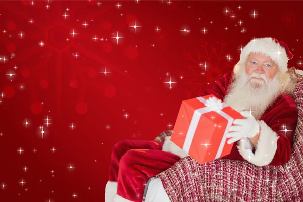 Father christmas offering a red gift — Stock Photo, Image