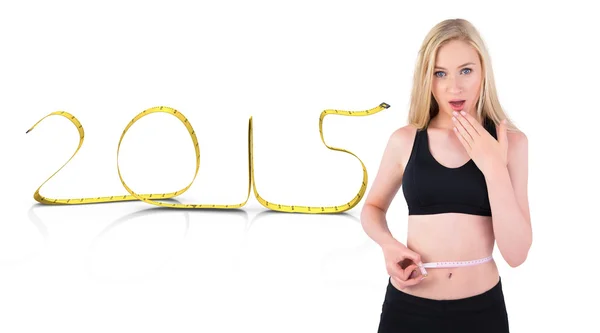 Composite image of fit young blonde looking at measuring tape — Stock Photo, Image