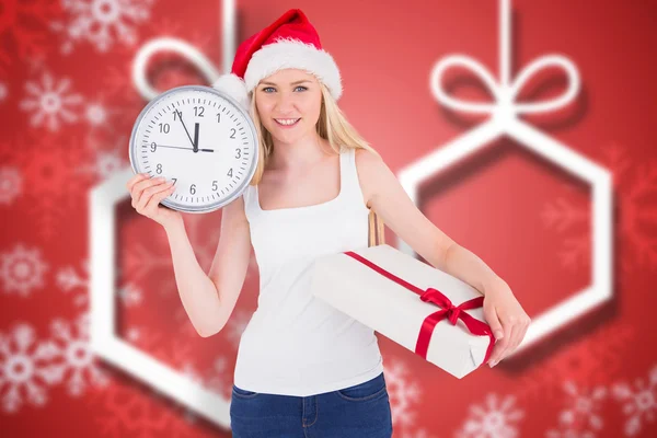 Composite image of festive blonde holding a clock and gift — Stock Photo, Image