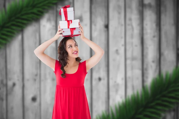 Composite image of happy brunette in red dress holding many gift — Stock Photo, Image