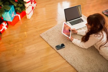Pretty woman lying on floor using technology at Chritmas clipart