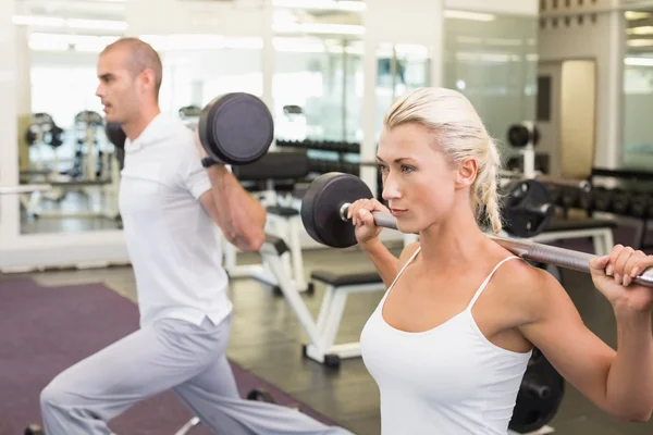 Deportiva joven pareja levantando barras en el gimnasio — Foto de Stock