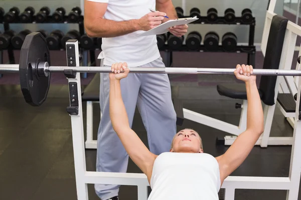 Entraîneur avec presse-papiers en plus femme levant haltère dans la salle de gym — Photo