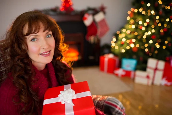 Sonriente pelirroja sosteniendo regalo en el sillón en Navidad —  Fotos de Stock