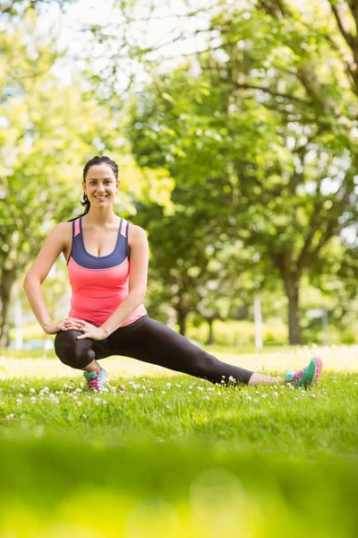 Happy fit brunette stretching on grass — Stock Photo, Image