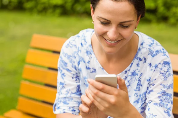 Smiling brunette sitting on bench texting — Stock Photo, Image