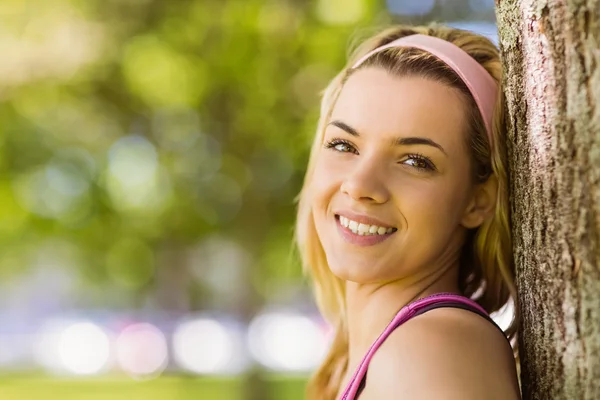 Fitte Blondine lehnt lächelnd an Baum — Stockfoto