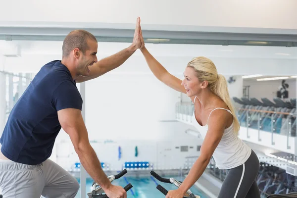 Couple giving high five on exercise bikes — Stock Photo, Image