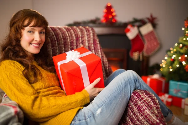 Smiling redhead holding gift on the couch at christmas — Stock Photo, Image