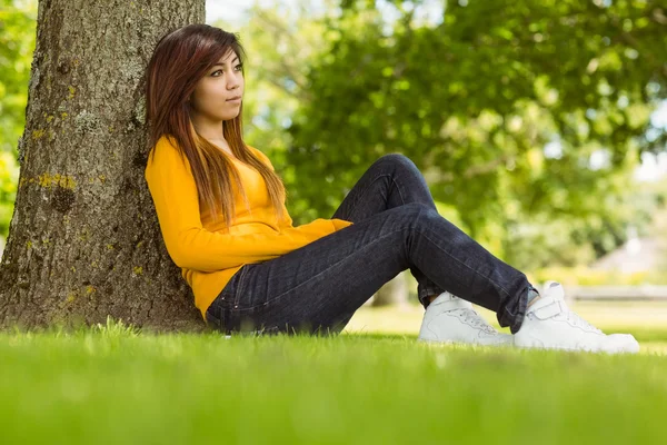 Žena sedí proti strom v parku — Stock fotografie