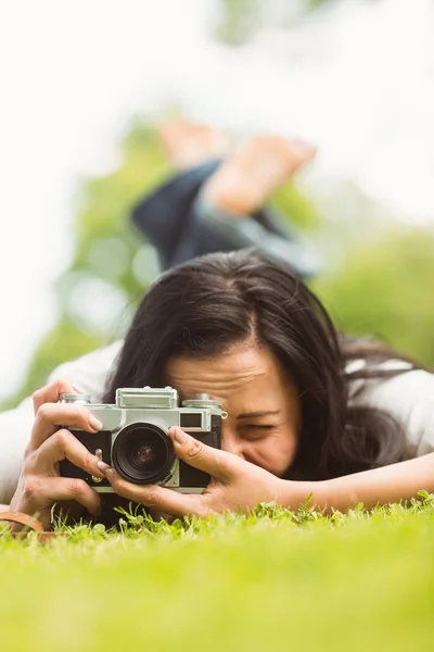 Brunette lying on grass with retro camera taking picture — Stock Photo, Image