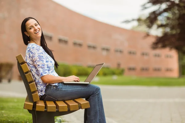 Glückliche braune Haare sitzen auf Bank mit Laptop — Stockfoto