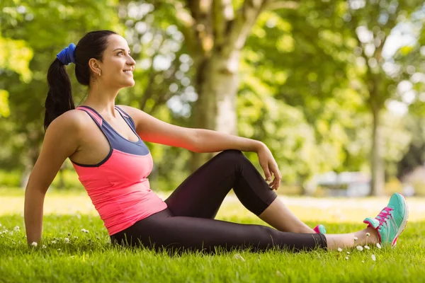 Cheerful fit brunette day dreaming on the grass — Stock Photo, Image