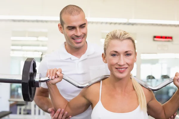 Allenatore aiutare la donna con sollevamento bilanciere in palestra — Foto Stock