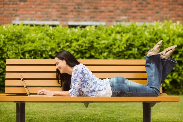 Cool brunette makaa penkillä kannettavan tietokoneen avulla — kuvapankkivalokuva