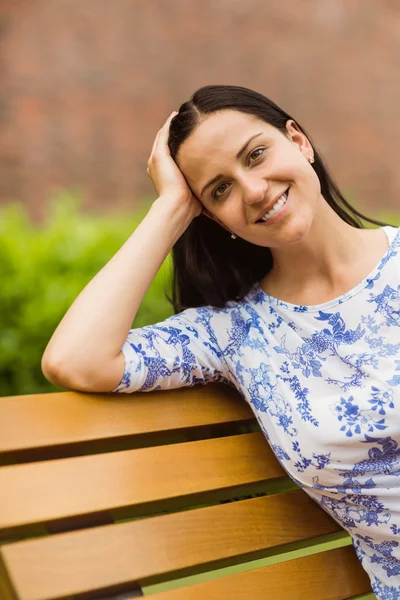 Brune souriante assise sur un banc regardant la caméra — Photo