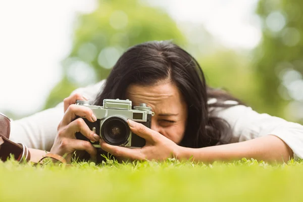 Morena acostada en la hierba tomando fotos con cámara retro — Foto de Stock