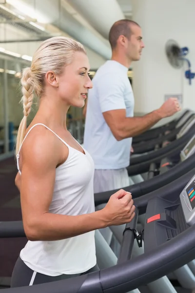 Seitenansicht eines Paares, das im Fitnessstudio auf Laufbändern läuft — Stockfoto