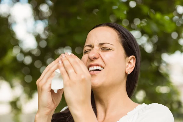 Sick brunette holding tissue sneezing — Stock Photo, Image