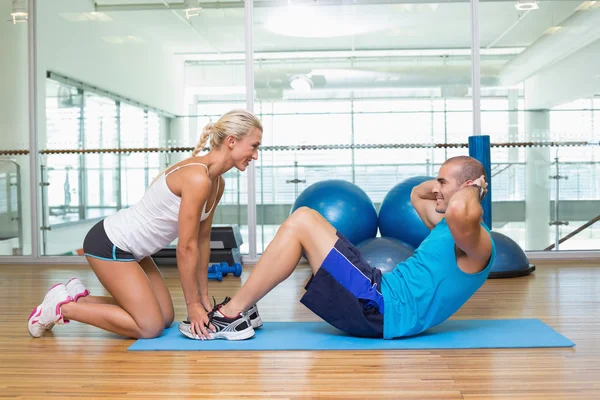 Trainer hilft jungem Mann bei Bauchkrämpfen im Fitnessstudio — Stockfoto