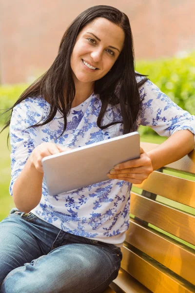 Morena sorridente sentada no banco usando tablet — Fotografia de Stock