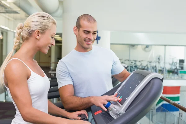 Entrenador ayudando a la mujer con opciones de pantalla de cinta de correr en el gimnasio — Foto de Stock