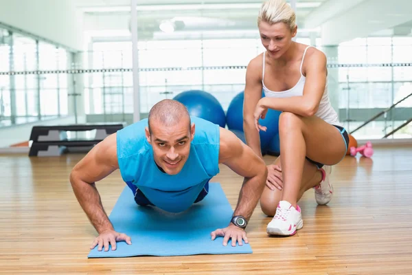 Trainer assisting man with push ups at gym — Stock Photo, Image