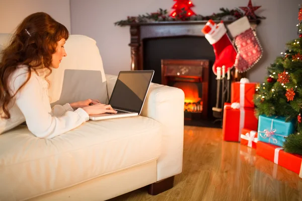 Mujer pelirroja sonriente usando el ordenador portátil en el sofá en Navidad —  Fotos de Stock