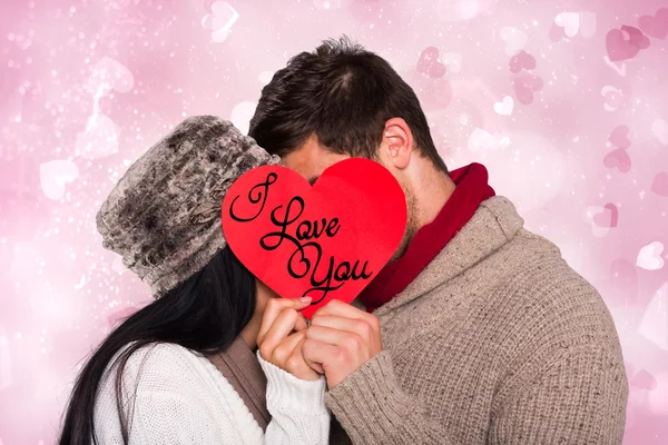 Young couple kissing behind red heart — Stock Photo, Image