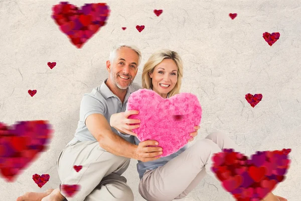 Happy couple sitting and holding heart pillow — Stock Photo, Image