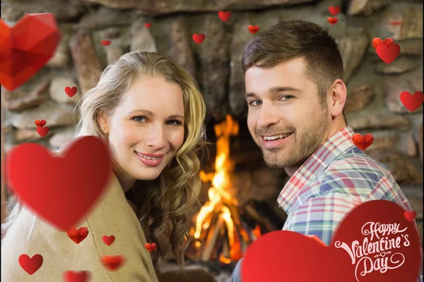 Smiling young couple in front of lit fireplac — Stock Photo, Image